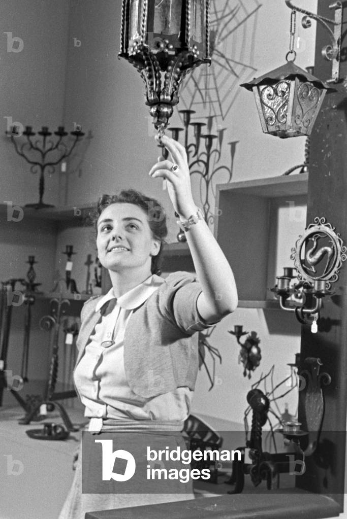Female staff member on a booth for lamps and illumination with exhibits, Germany 1940s (b/w photo)