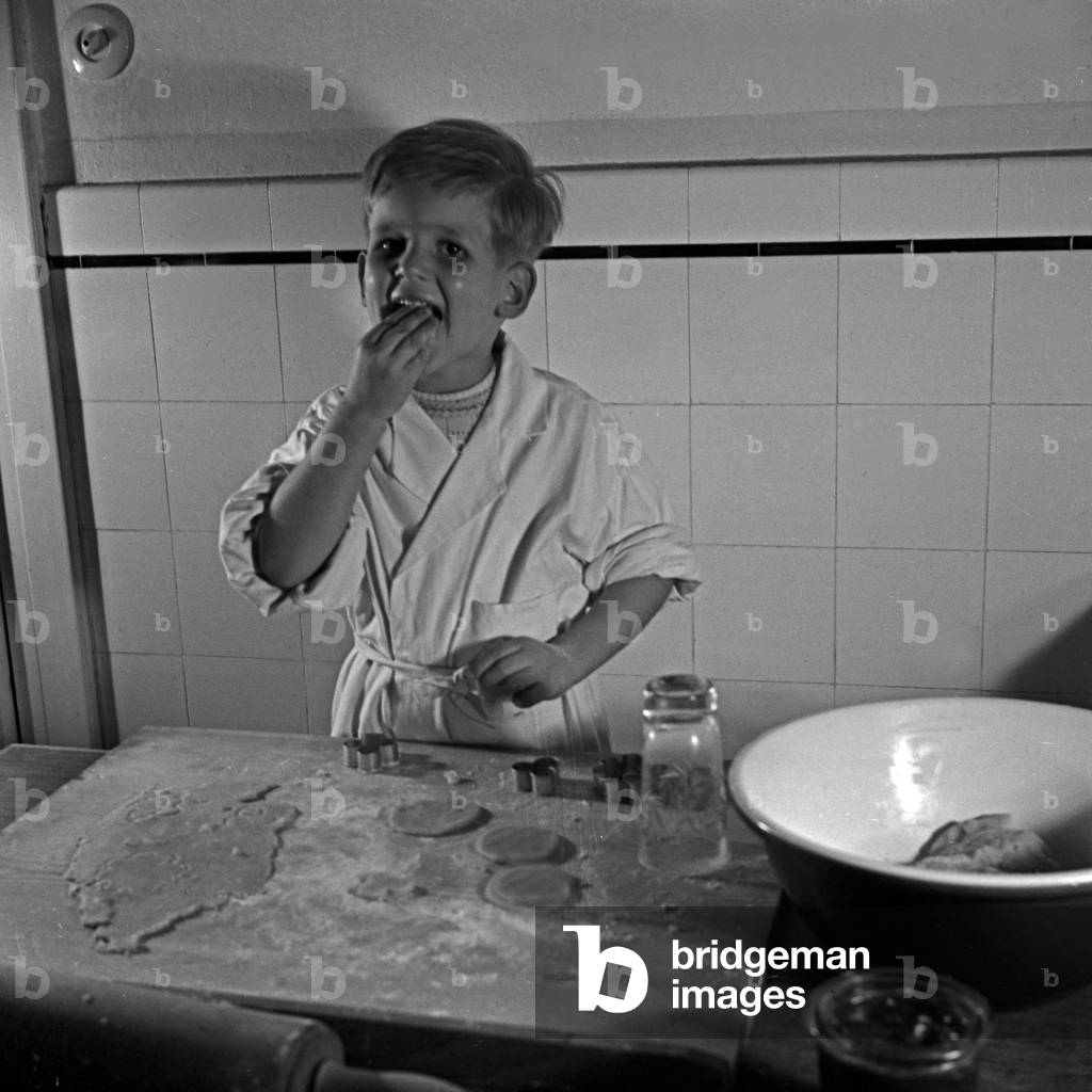 A little boy nibbling dough for christmas cookies, Germany 1930s (b/w photo)