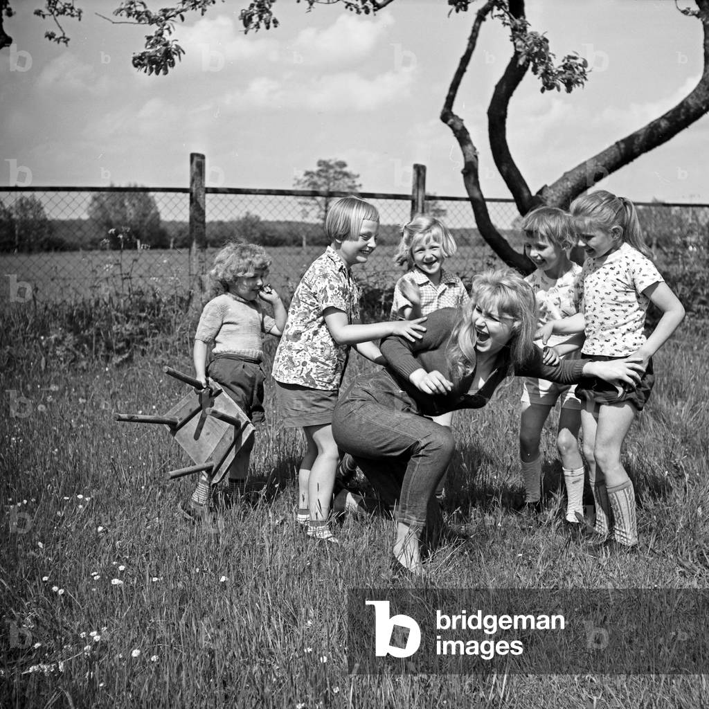 German actress Karin Stoltenfeldt helping playing with children in the garden, Germany 1950s