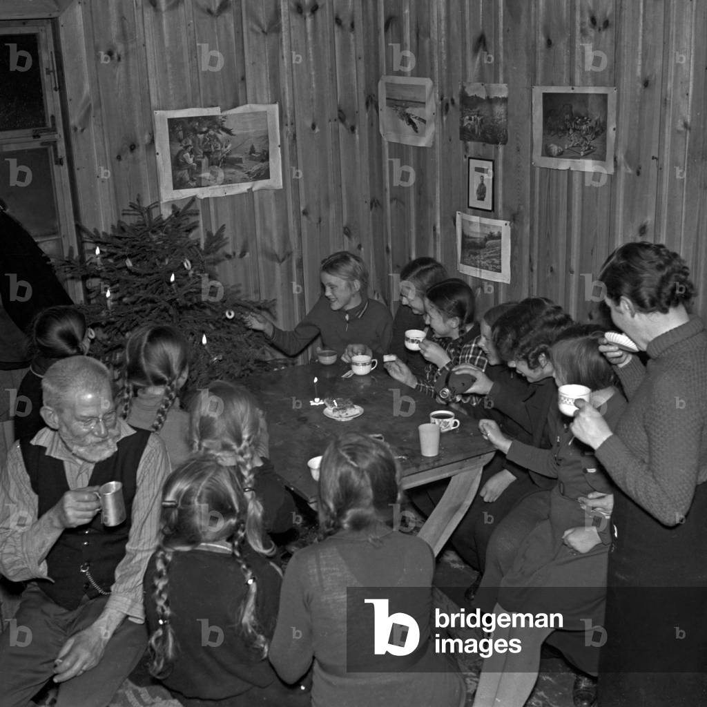 A cup of hot tea warms up everyone for trimming the christmas tree, Germany 1930s (b/w photo)