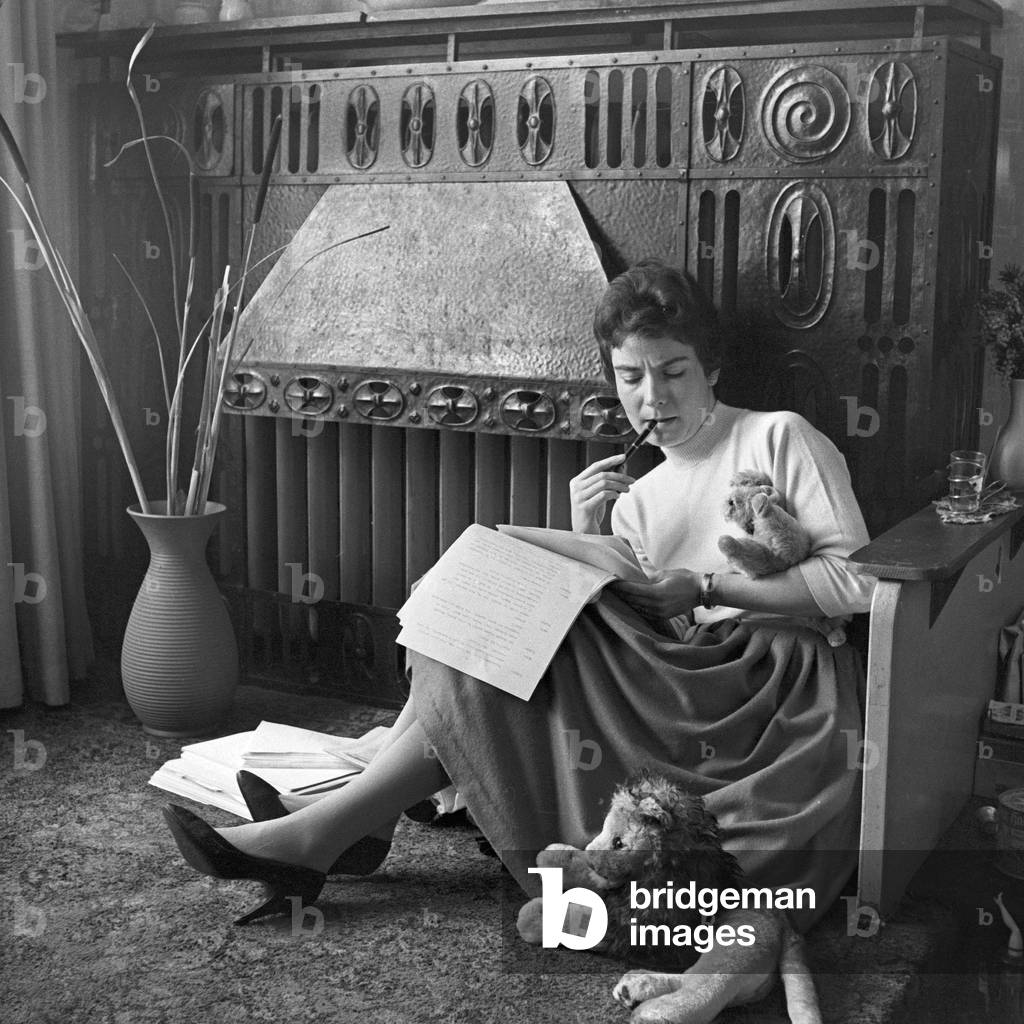 German schlager singer Melitta Berg sitting with plush toys by the fireplace and learning at Hamburg, Germany 1950s