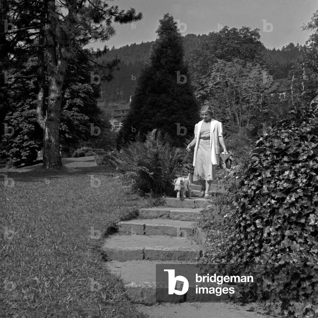 A woman walking her fox terrier in a public park at Wildbad in Black Forest, Germany 1930s (b/w photo)
