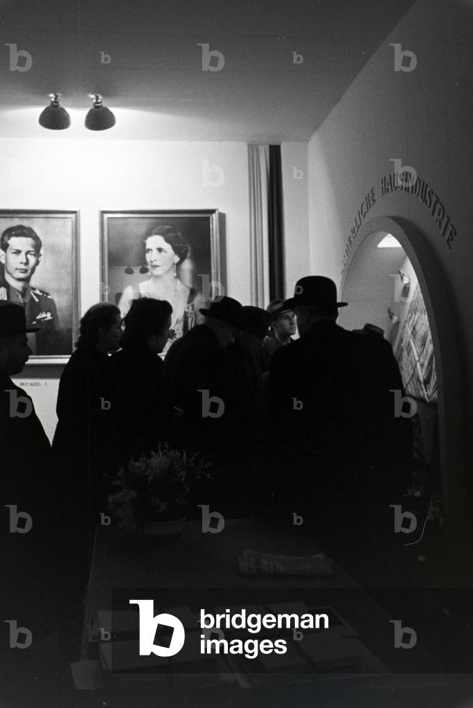 Visitors of the Leipziger Frühjahrsmesse at a Romanian stand with portraits of the Romanian King Michael I and his mother Elena of Greece, Germany 1941 (b/w photo)