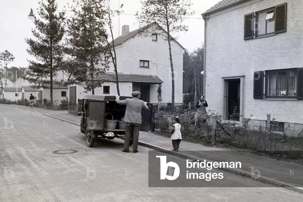 A man is delivering and selling groceries on the street to the residents of the zeppelin village near Frankfurt am Main with the help of a little car, Germany 1930s (b/w photo)