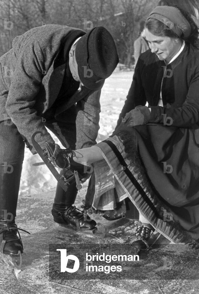 A man helping a woman to put on ice skate runners at Spreewald area, Germany 1930s (b/w photo)