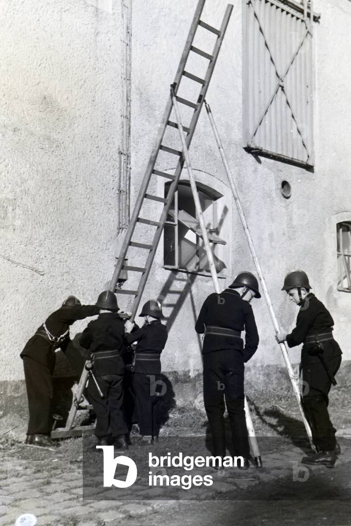 A group of junior firefighters is preparing a ladder during a firefighter training, Germany 1930s (b/w photo)