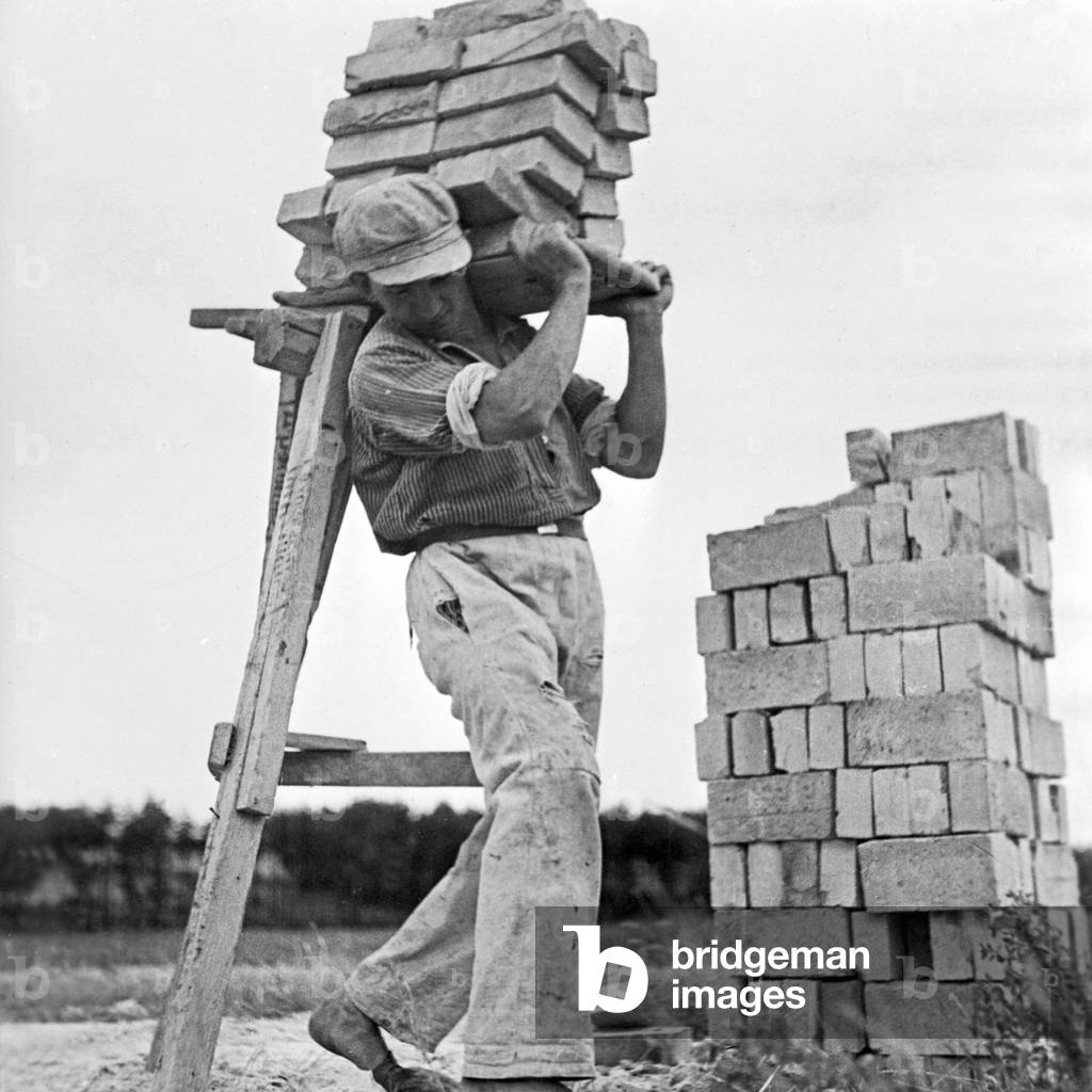 A construction worker carrying a load of bricks, Germany 1930s (b/w photo)