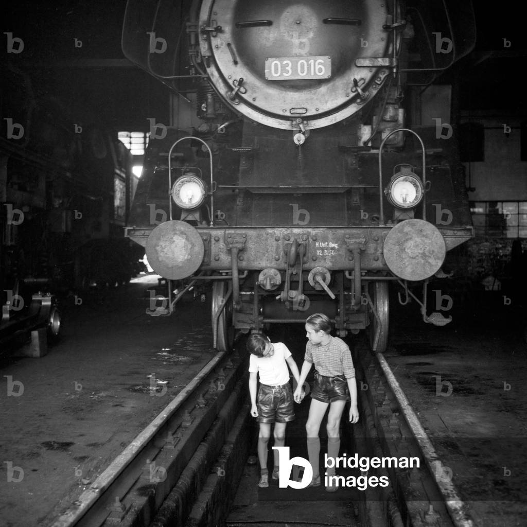 Two boys at a slag pit in front of a steam engine of type 03 in an engine shed at Hamburg depot, Germany 1950s
