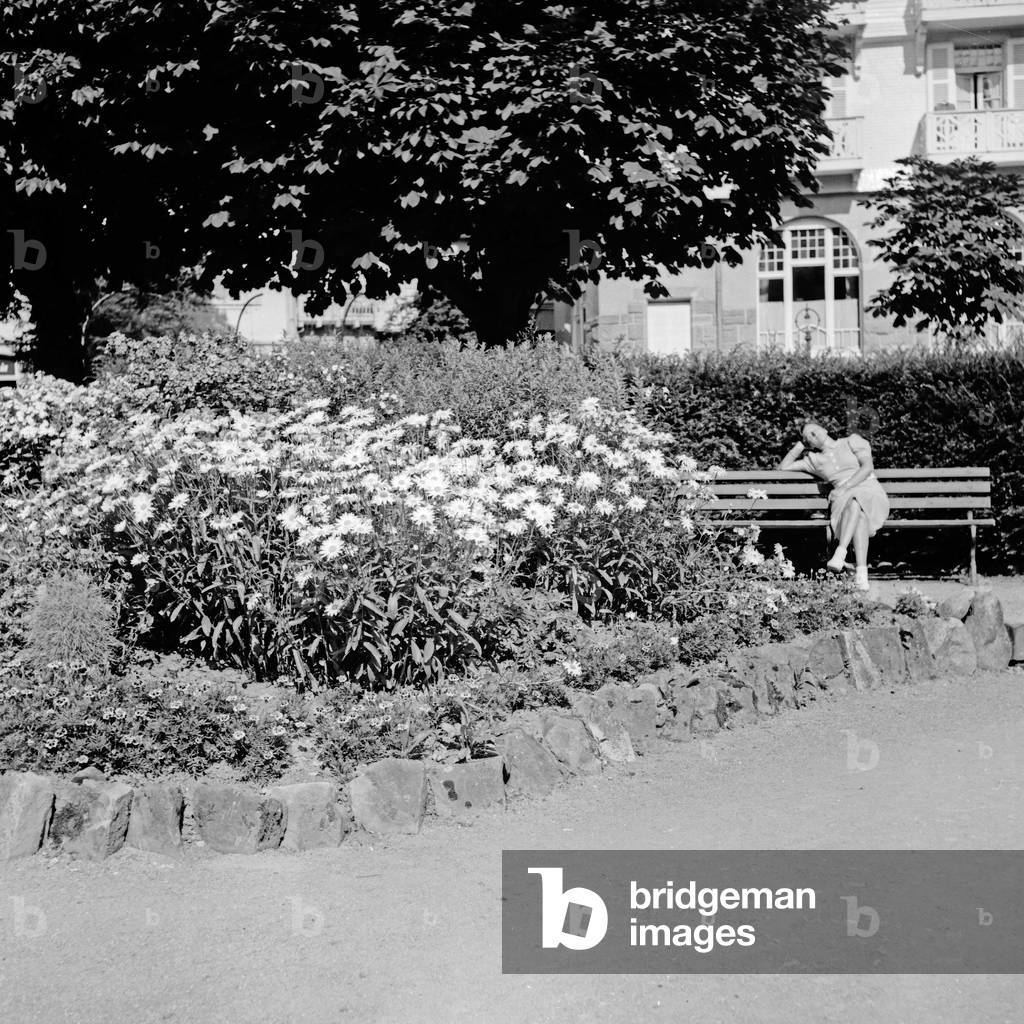 A woman sitting on a bench at a public garden, Germany 1930s (b/w photo)