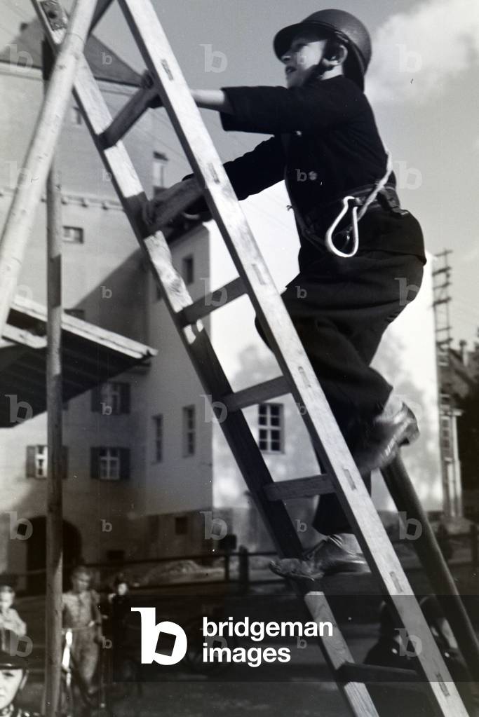A boy of the junior firefighters is climbing up a ladder during a firefighter training, Germany 1930s (b/w photo)