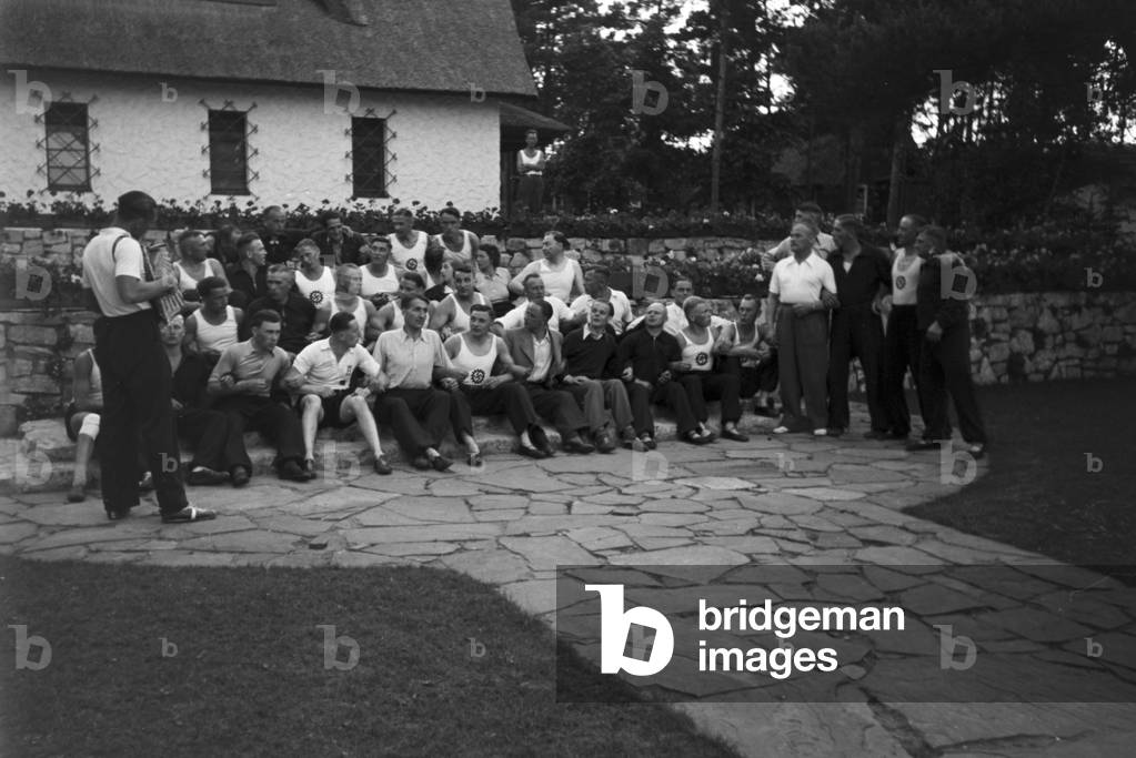 People singing and dancing in front of forest huts at the sports club at Belzig in Brandenburg, Germany 1930s (b/w photo)