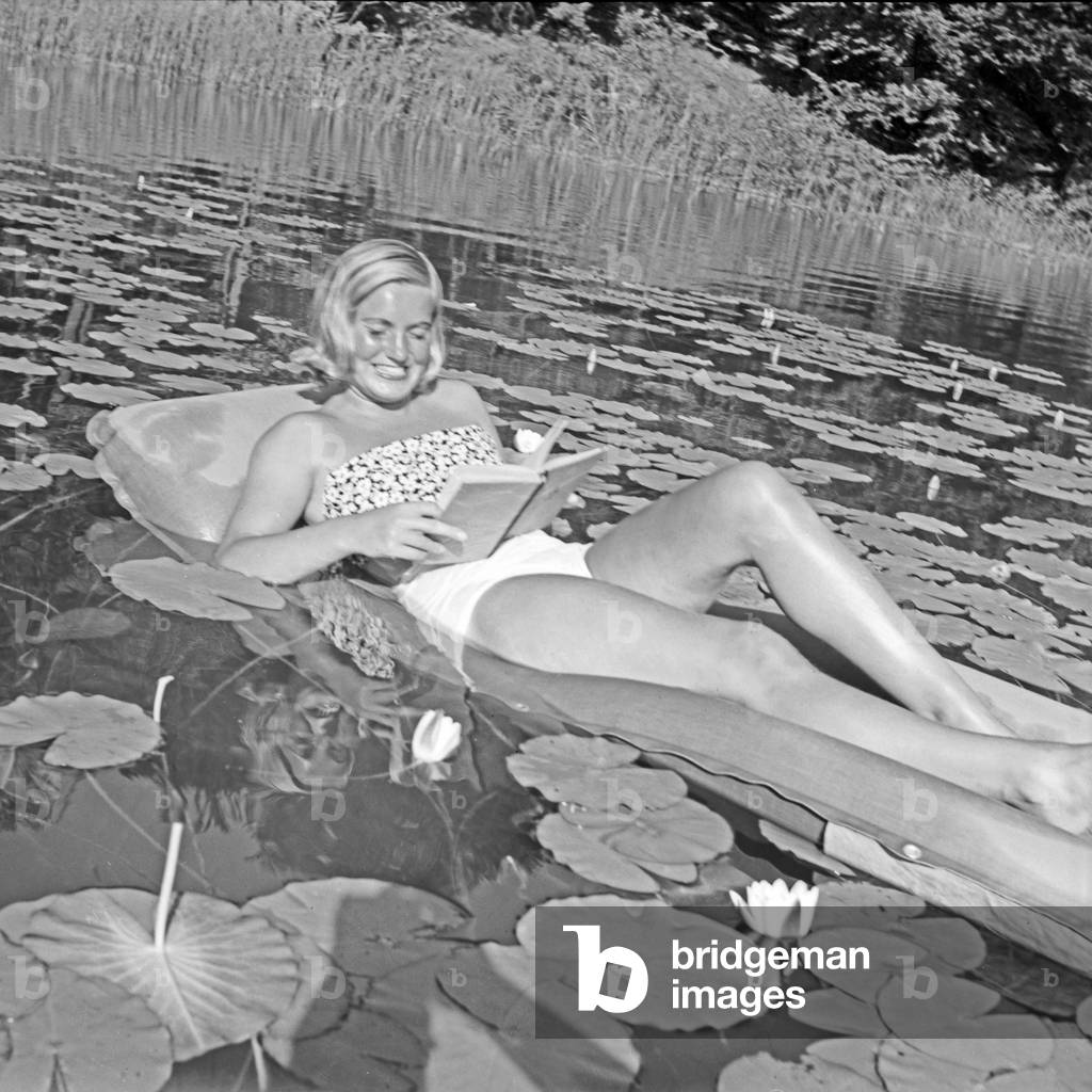 A young woman relaxing on an air mattress on a pond full of water lilies, Germany 1930s (b/w photo)