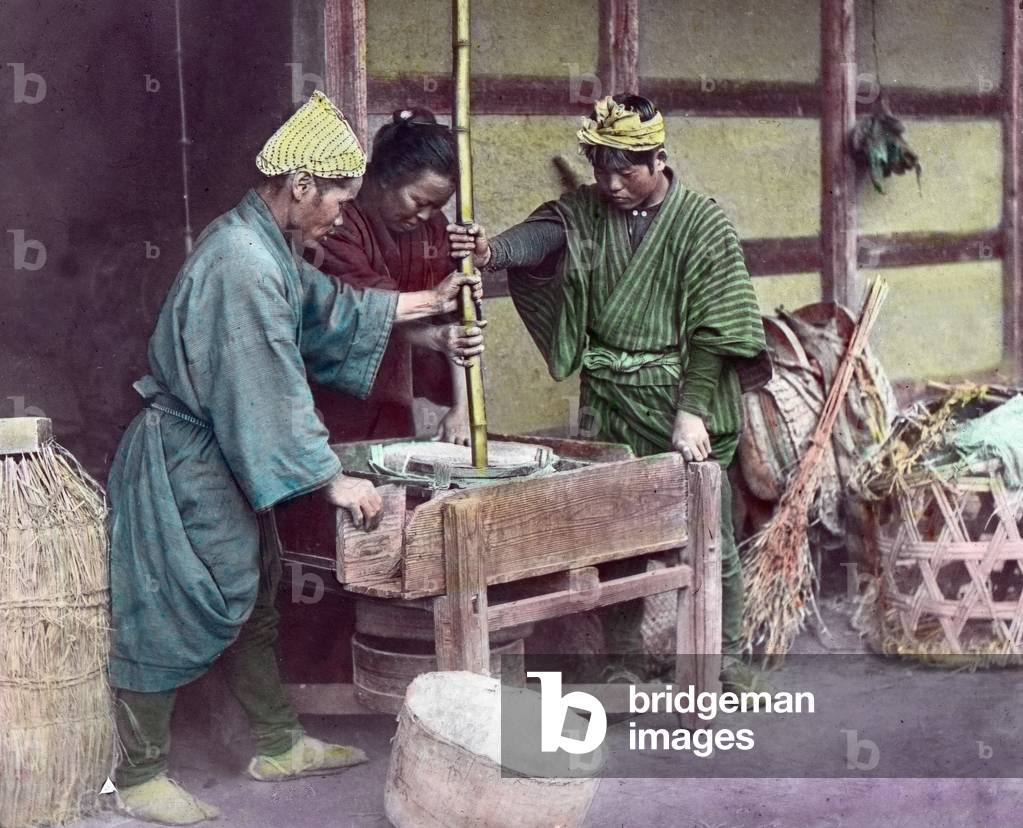 Japan, farmer family grinding the grain in a hand-mill at home, image date: circa 1920. Carl Simon Archive