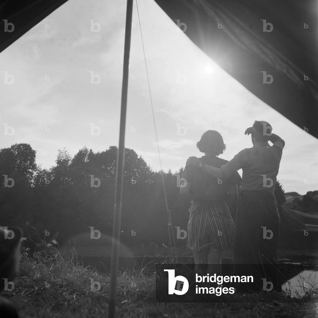 A man and a woman standing in front of their tent and watching the sunset, Germany 1930s (b/w photo)