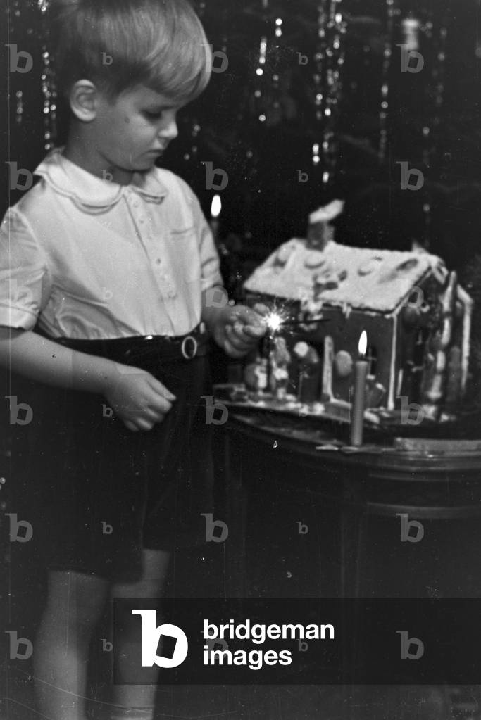 A boy lighting a candle at Christmas, Germany 1930s (b/w photo)