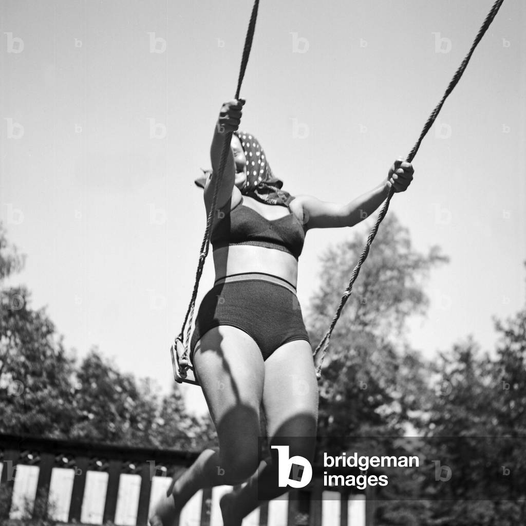 A young woman wearing a bikini on a swing on a playground in the Wachau area in Austria, Germany 1930s (b/w photo)