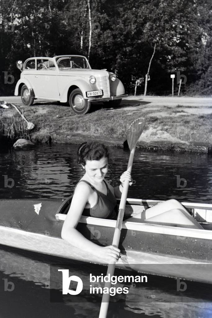 Young woman paddling in a boat on a lake near the river, Germany 1930s (b/w photo)