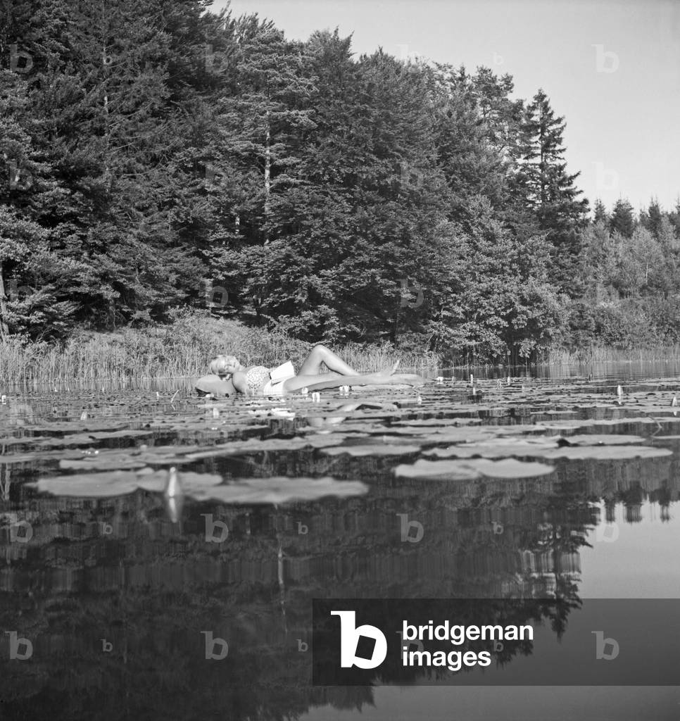 A young woman on an air matress on a lake in the Wachau area in Austria, Germany 1930s (b/w photo)
