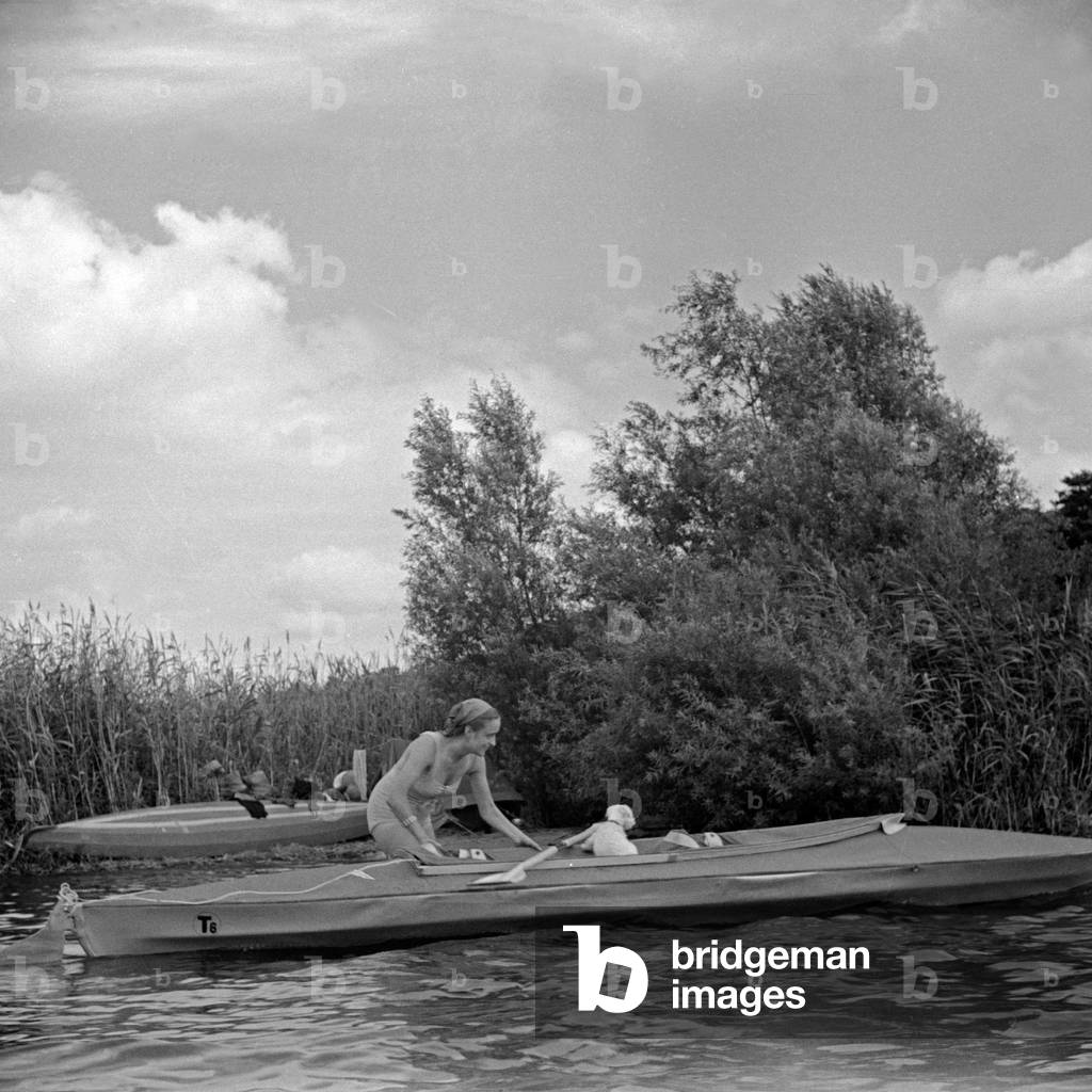 Advertising für a Klepper foldboat: a young woman playing with a puppy paddling on the shore of a lake, Germany 1930s (b/w photo)