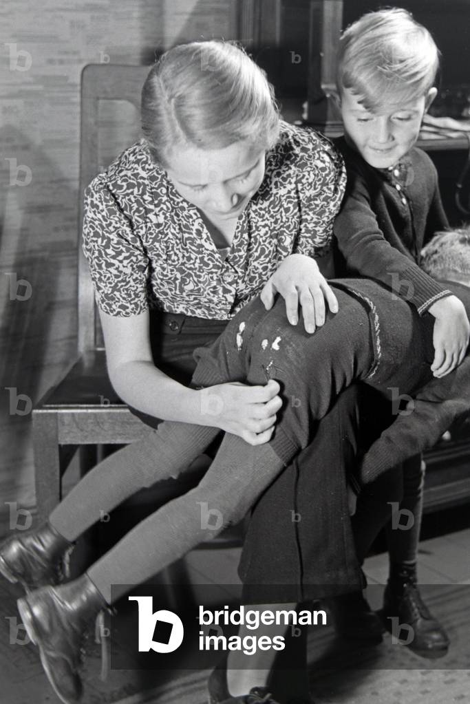 The eldest daughter of a extended family repairing the trousers of her little brother, Germany 1930s