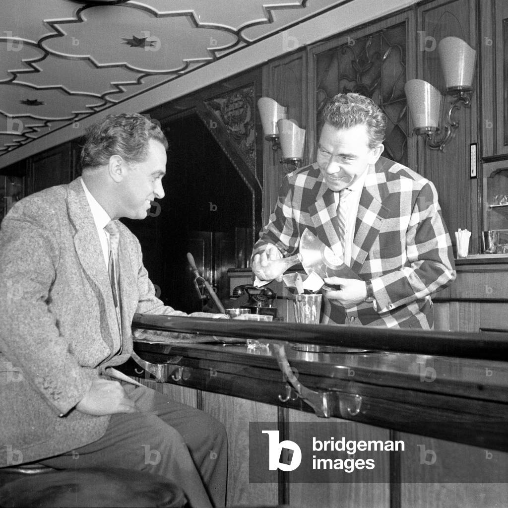 German entertainer and show presenter Peter Frankenfeld mixing and serving a cocktail to a guest of a hotel bar, Hamburg 1954