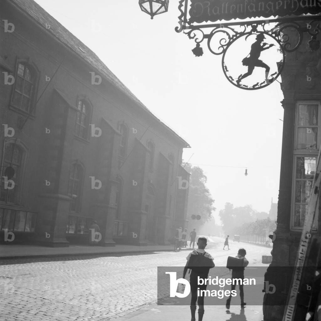 School kids in front of a house with the Pied Piper's symbol at the old city of Hameln on river Weser, Germany 1930s (b/w photo)
