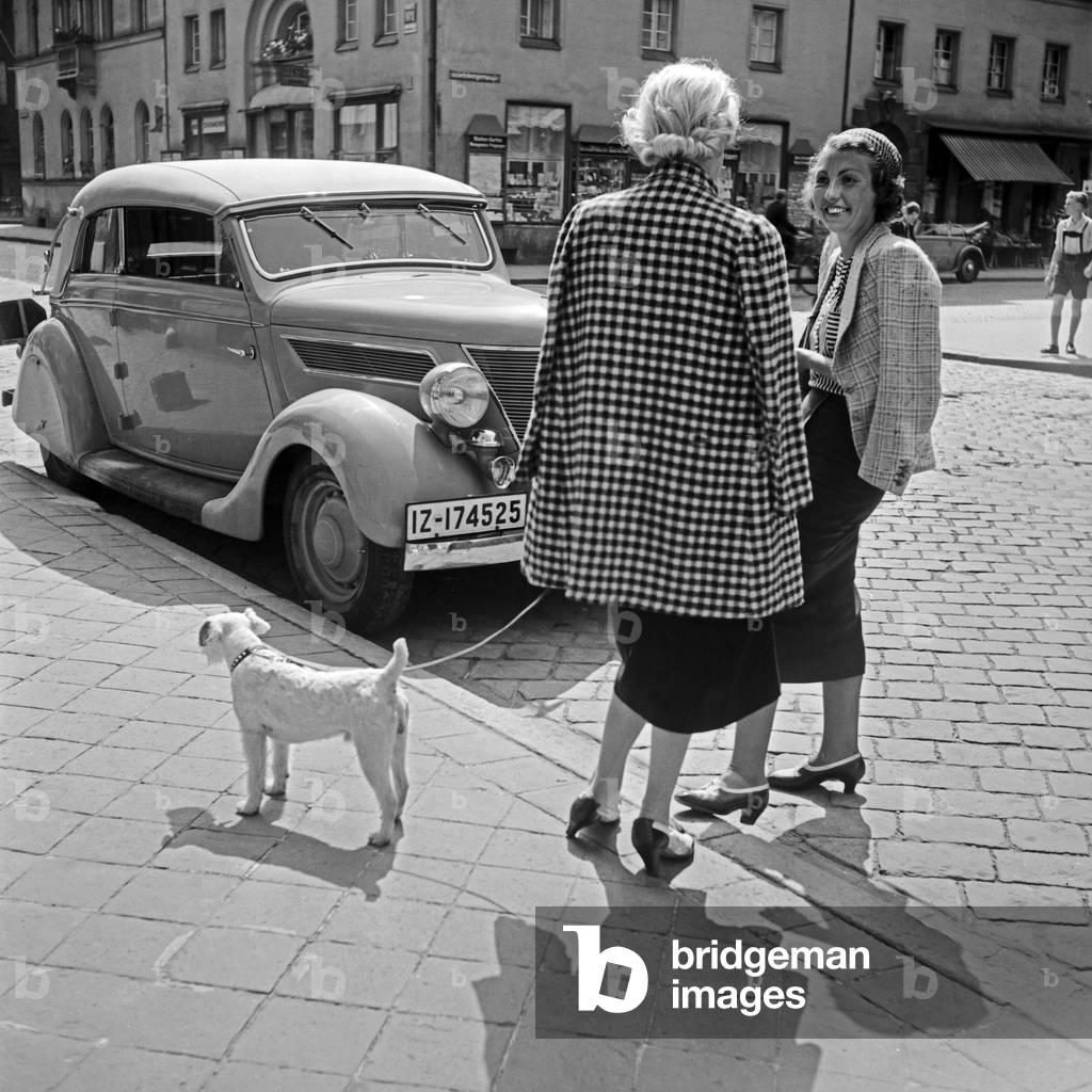 Two women at Miesbach chatting with her dog in front of a Ford V8 convertible, Germany 1930s (b/w photo)