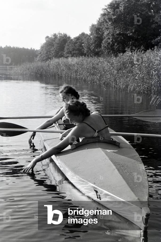 Two young women in bathing suits are paddling in a boat, Klepper T6 on a lake, Germany 1930s (b/w photo)