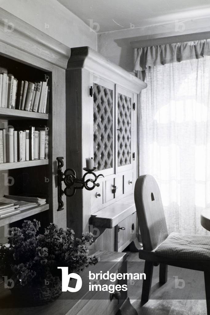 Living room with a bookshelf and wooden furniture in Hartmannsberg castle, the residence of sculptor Josef Thorak, Germany 1930s (b/w photo)