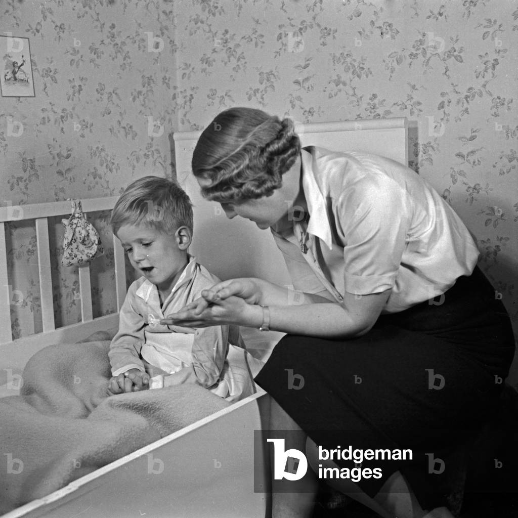 A mother bringing her son to bed and listening to his daily adventures, Germany 1930s (b/w photo)
