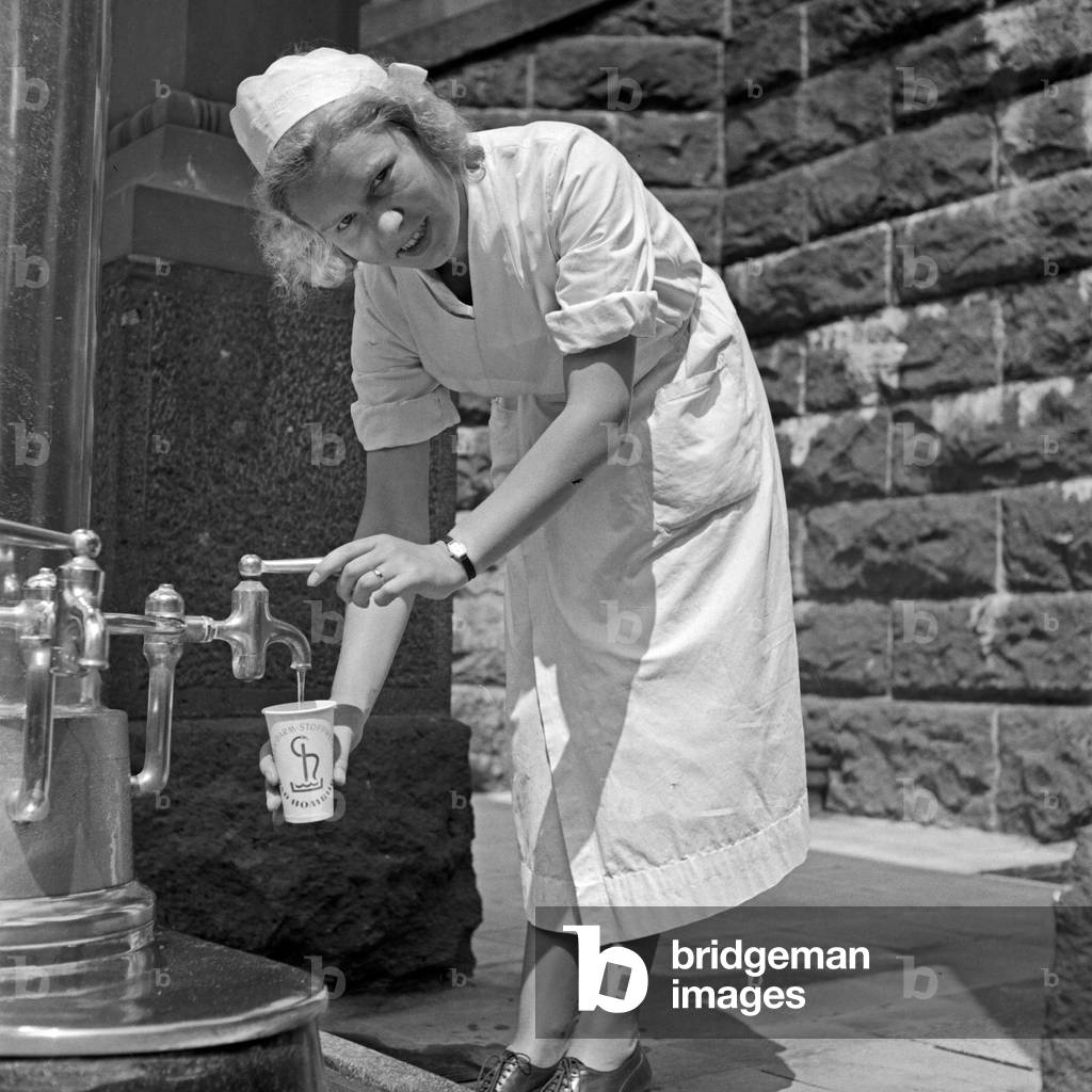 A nurse on a well of healing water at Bad Homburg spa resort, Germany 1930s (b/w photo)