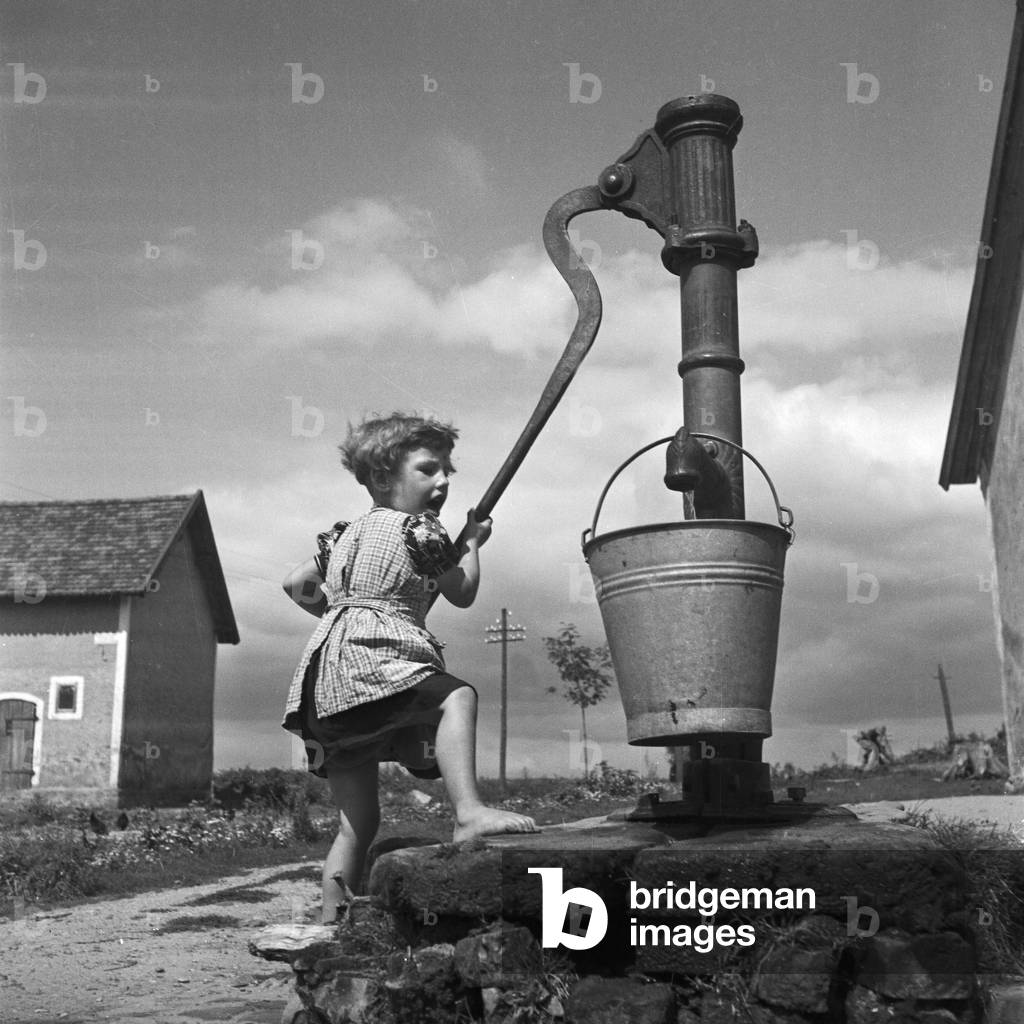 A girl taking water from a well at Allenstein in East Prussia, Germany 1930s (b/w photo)