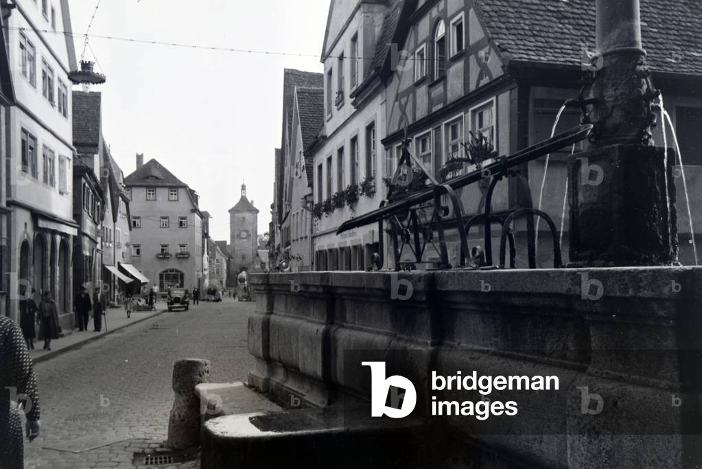 A street lined with half-timbered buildings and a fountain in Rothenburg ob der Tauber, Germany 1930s (b/w photo)