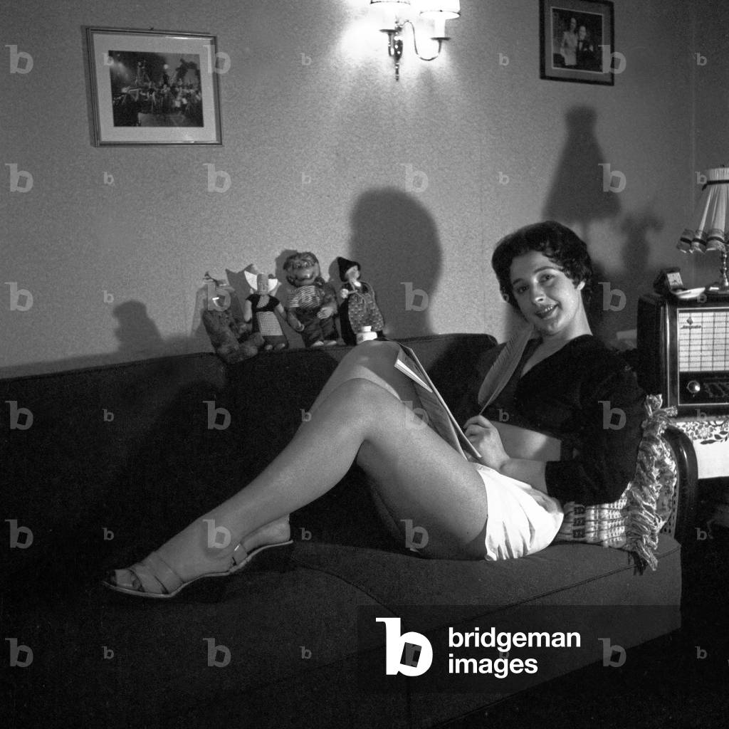 German schlager singer Renee Franke sitting on the sofa with her dolls, Hamburg 1956