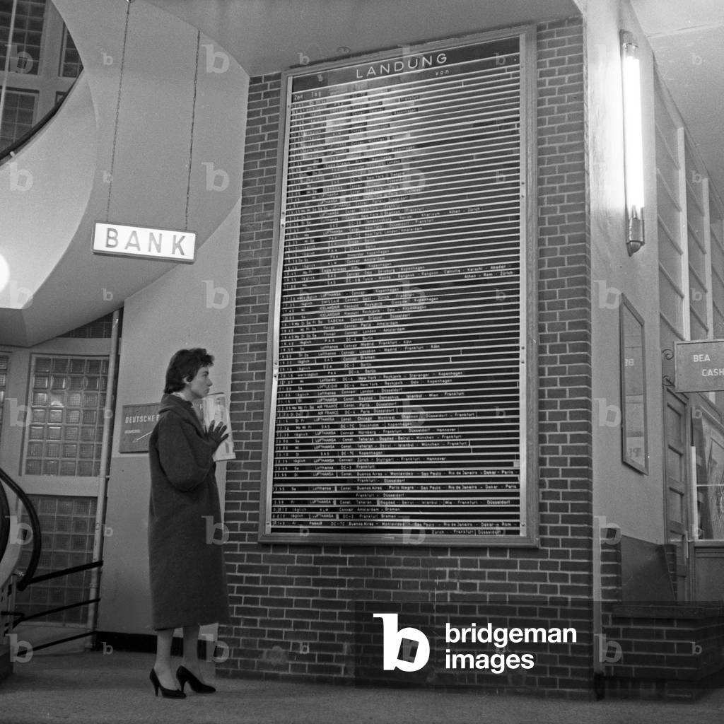 German schlager singer Melitta Berg with a Burda magazine at the destination board of Hamburg airport, Germany 1950s