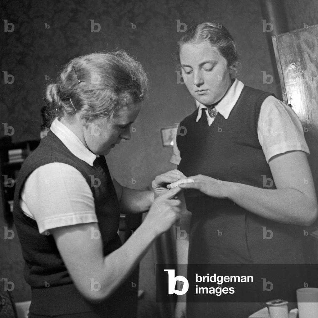 Two women at a First Aid from a small housekeeping disaster at the female workforce group of Molkenberg, Germany 1930s (b/w photo)
