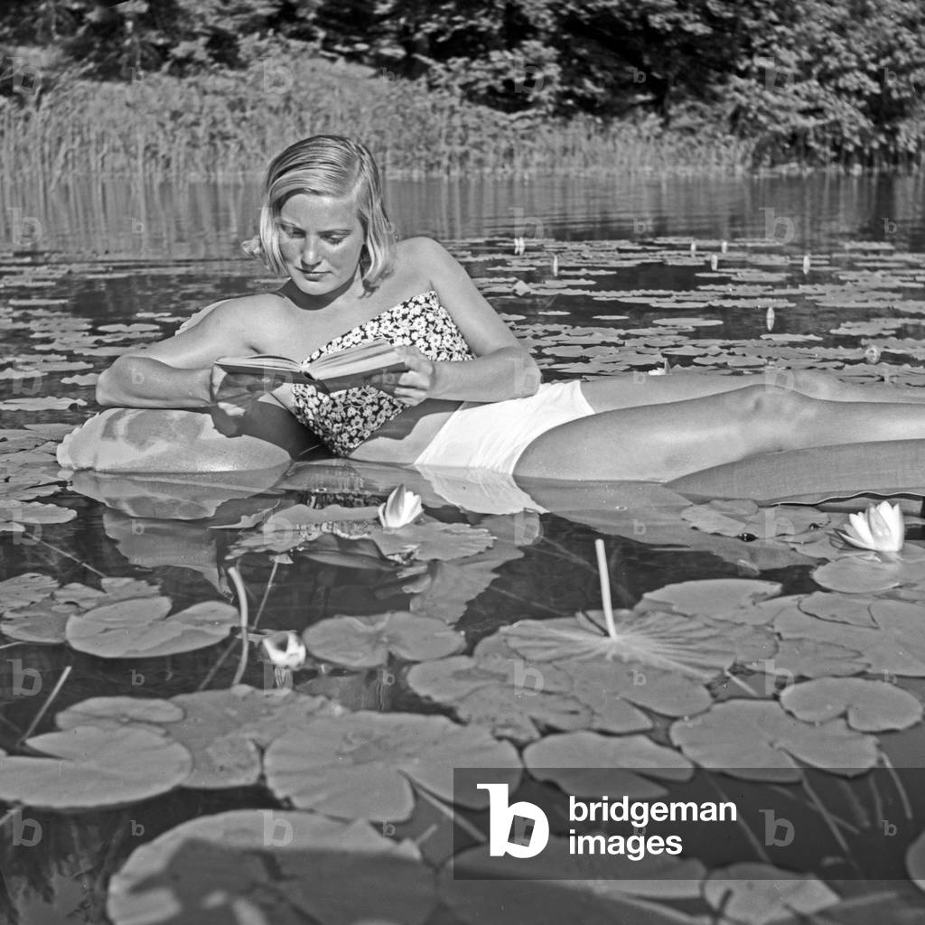 A young woman relaxing on an air mattress on a pond full of water lilies, Germany 1930s (b/w photo)