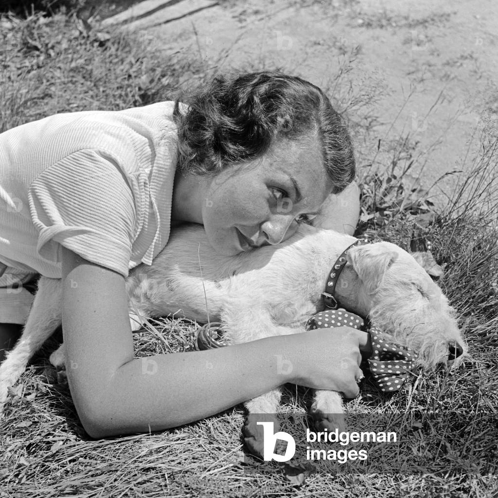 A young woman sitting in a lawn with her fox terrier pup, Germany 1930s (b/w photo)