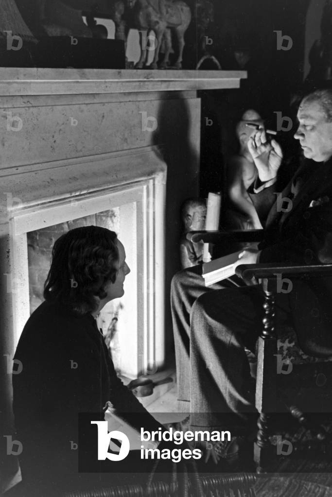 German actor Paul Wegener smoking a cigar while sitting by the fireside with his wife, actress Greta Schroeder, at his house in Berlin, Germany 1930s (b/w photo)