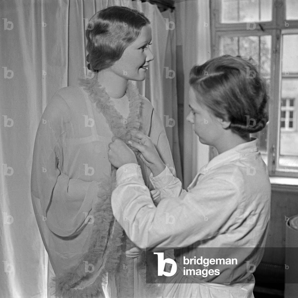A woman dressing up a Kaethe Kruse display dummy at Bad Kosen, Germany 1930s (b/w photo)