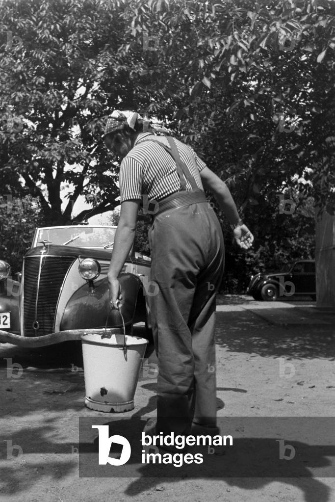 A young woman washing a Ford model Eifel, Germany 1930s (b/w photo)