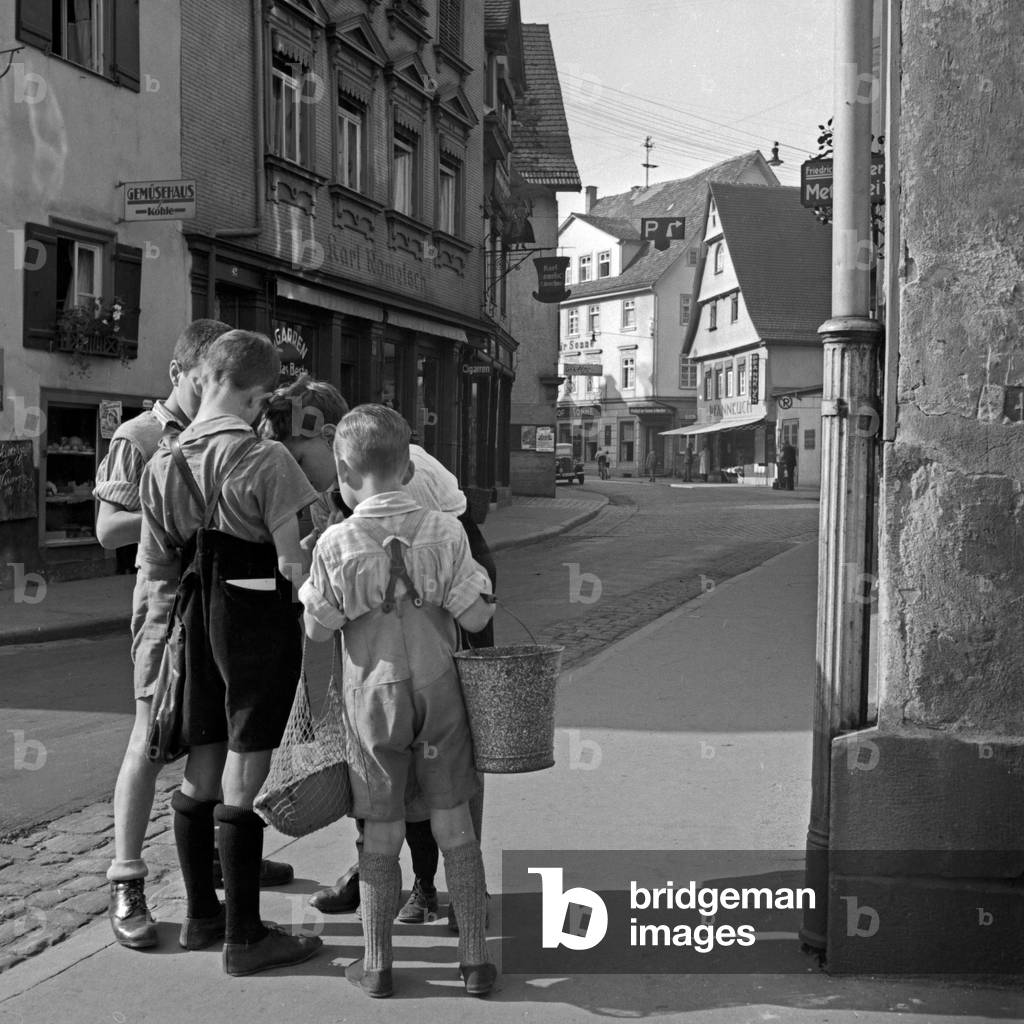 Four boys at the street in front of Karl Rometsch's furrier workshop and Koehle's greengrocery shop at the town of Wildbad in Black Forest, Germany 1930s (b/w photo)