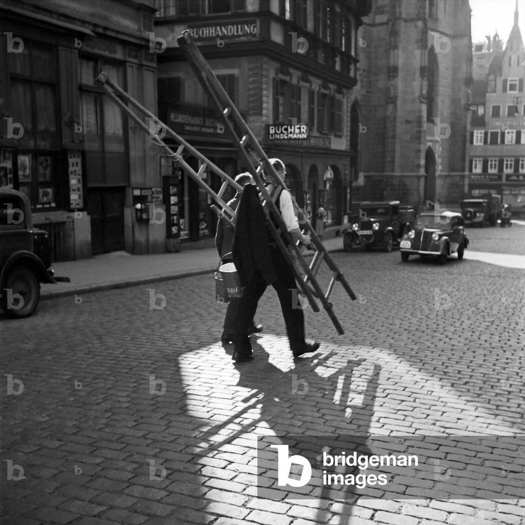 Two painters or window cleaners crossing the street in front of Lindemann's book store at Stuttgart, Germany 1930s (b/w photo)