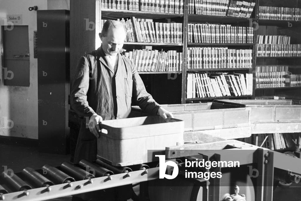 A librarian of the Berlin State Library (former Prussian State Library) at the book conveyor system in the library magazine, Germany 1930s (b/w photo)