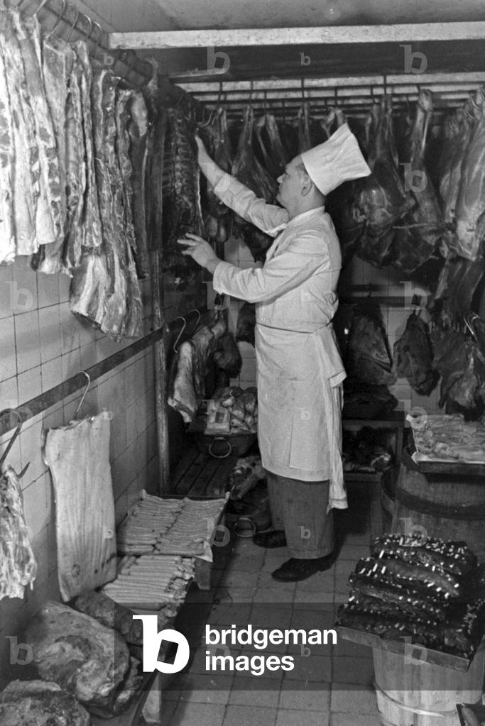 A chef with meat in the reefer of the kitchen of a restaurant, Germany 1930s (b/w photo)