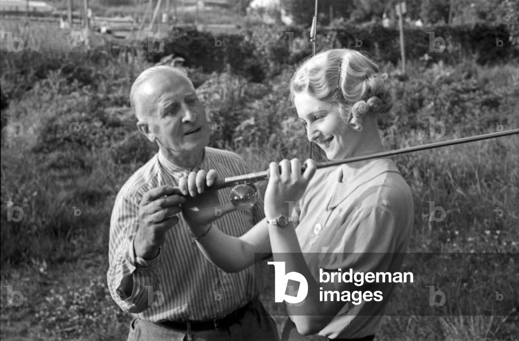 A woman listening and learning from her male competitors at an angling contest, Germany 1930s (b/w photo)