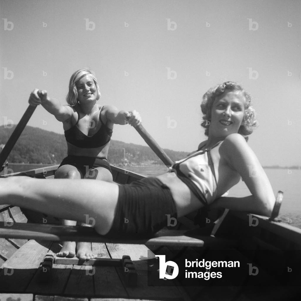 Two young women tanning in a boat on a lake at the Wachau area in Austria, Germany 1930s (b/w photo)