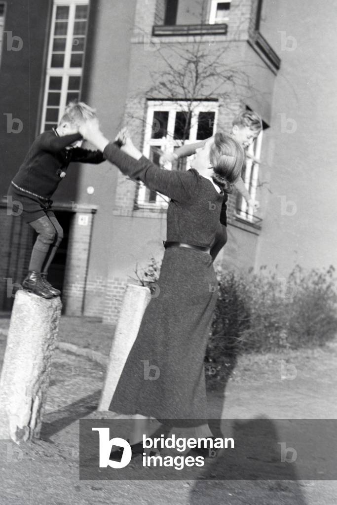 Members of an extended family playing in front of the apartment building , Germany 1930s (b/w photo)