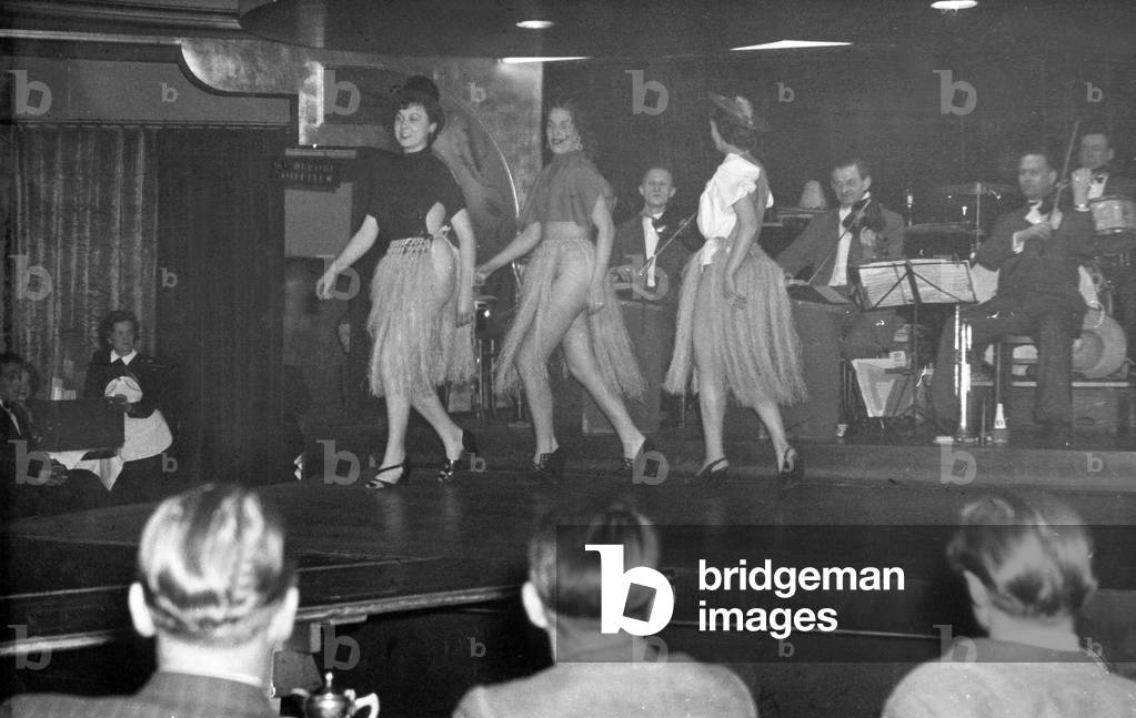 The audience follows the performance of three dancers on the stage of a nightclub at Hamburg Reeperbahn, 1950s
