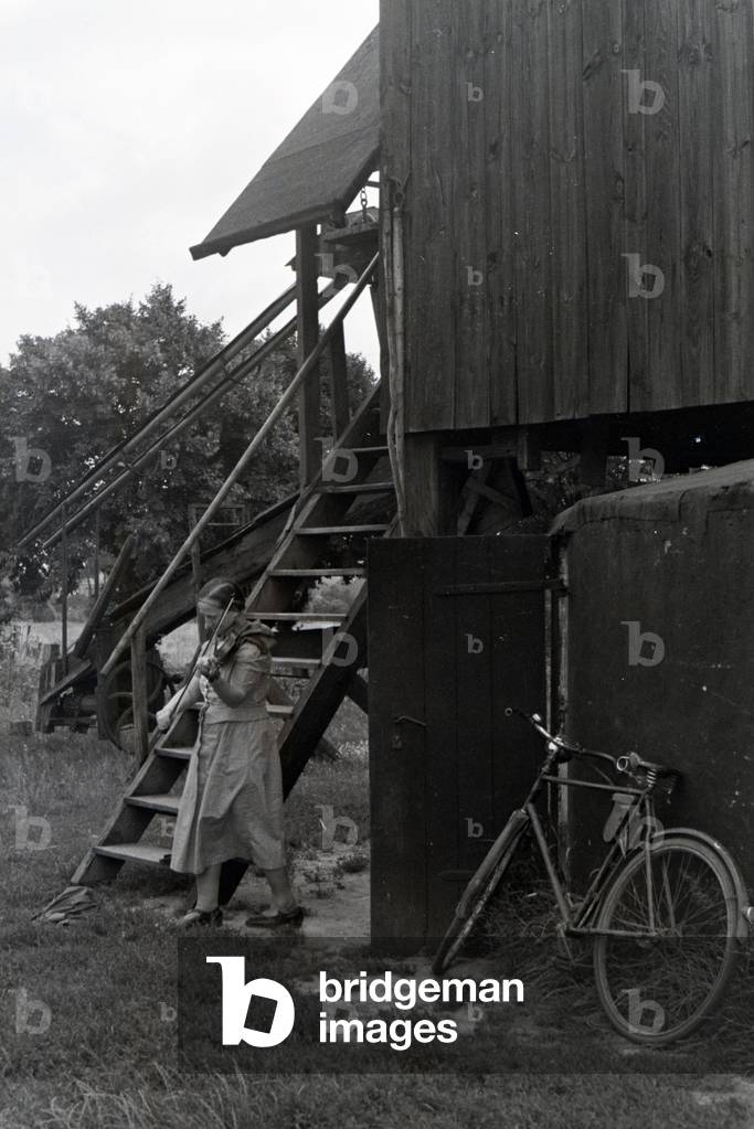 A woman playing violin while standing at the doorway of a wind mill, Germany 1930s (b/w photo)